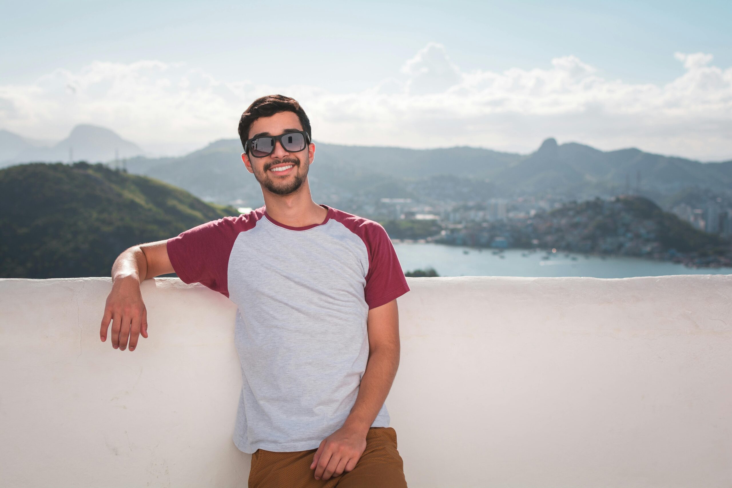 Testimonial Young man in sunglasses leaning on a balcony with a scenic city view in the background.