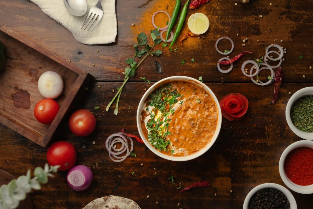 Home A vibrant top-down view of a flavorful Indian curry surrounded by fresh vegetables and spices.
