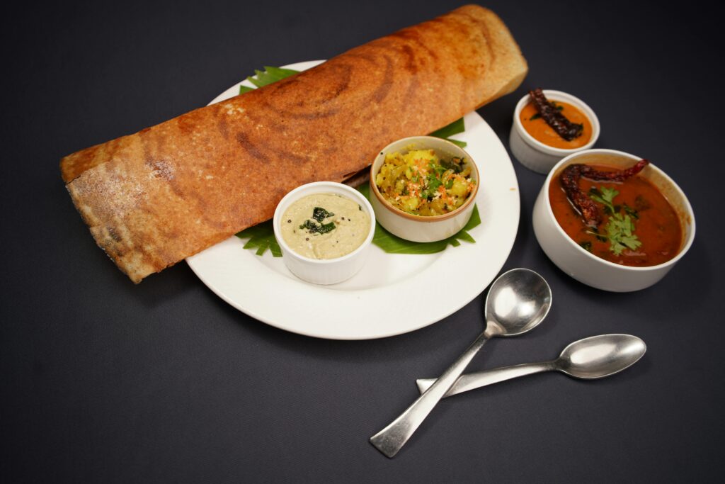 Home Crispy dosa served with coconut chutney, vegetable curry, and sambar on a black background.