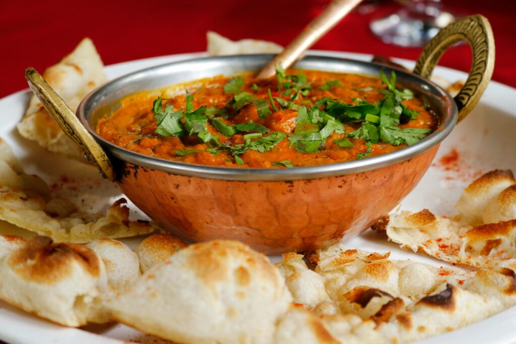 Home Delicious Indian curry garnished with cilantro served with naan in a copper dish.