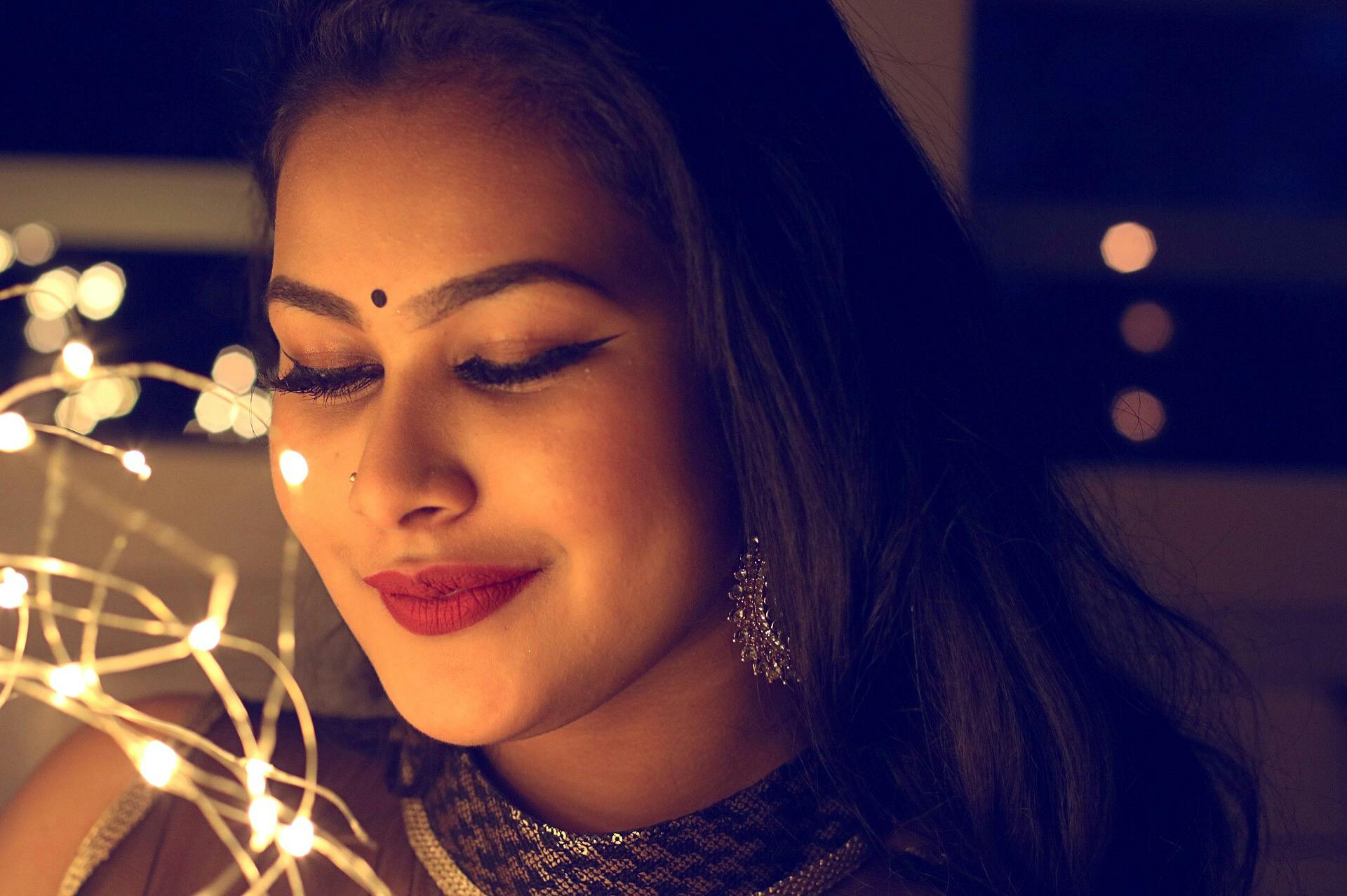 Testimonial Portrait of a smiling woman adorned with lights and elegant jewelry, creating a warm, glamorous atmosphere.